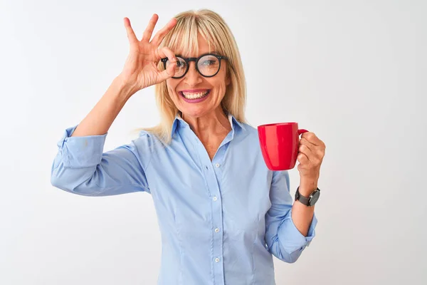 Middle age businesswoman wearing glasses drinking coffee over isolated white background with happy face smiling doing ok sign with hand on eye looking through fingers