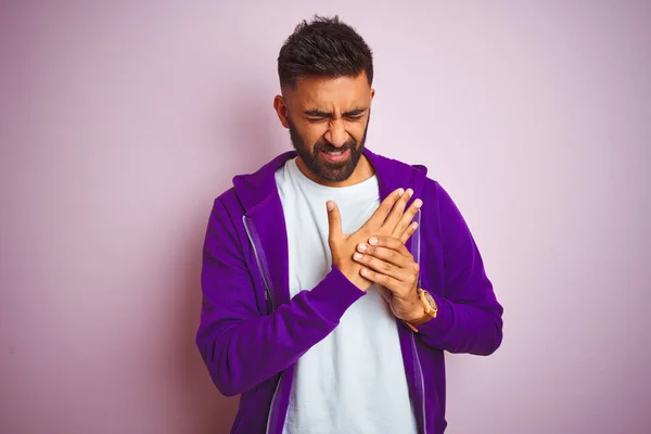 Young indian man wearing purple sweatshirt standing over isolated pink background Suffering pain on hands and fingers, arthritis inflammation
