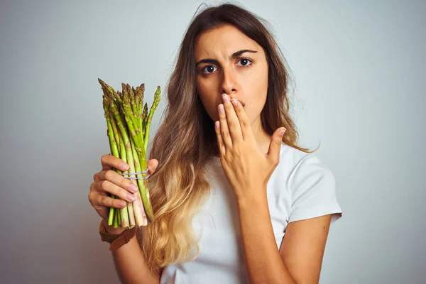 若い美しい女性食べるアスパラガスグレー隔離された背景カバー口で手でショックを受けた恥でミス 恐怖の表現 沈黙の中で怖がって 秘密の概念 — ストック写真