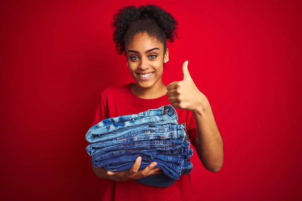 Young African American Woman Holding Stack Jeans Isolated Red Background — Stock Photo, Image