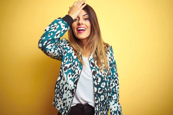 Young beautiful woman wearing casual jacket over yellow isolated background surprised with hand on head for mistake, remember error. Forgot, bad memory concept.