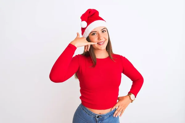 年轻美丽的女孩戴着圣诞圣诞礼帽 站在孤独的白色背景上微笑着 用手和手指做着电话手势 就像在电话里说话一样 交流概念 — 图库照片