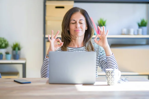 中年妇女坐在桌旁 用电脑笔记本电脑工作 闭上双眼微笑 用手指做冥想手势 瑜伽概念 — 图库照片