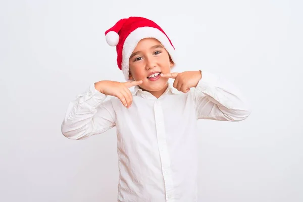 漂亮的小男孩戴着圣诞圣诞礼帽 站在孤独的白色背景上 笑容满面 用手指 牙齿和嘴指指指点点 牙齿健康概念 — 图库照片