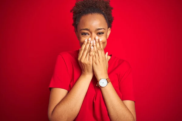 Young beautiful african american woman with afro hair over isolated red background laughing and embarrassed giggle covering mouth with hands, gossip and scandal concept