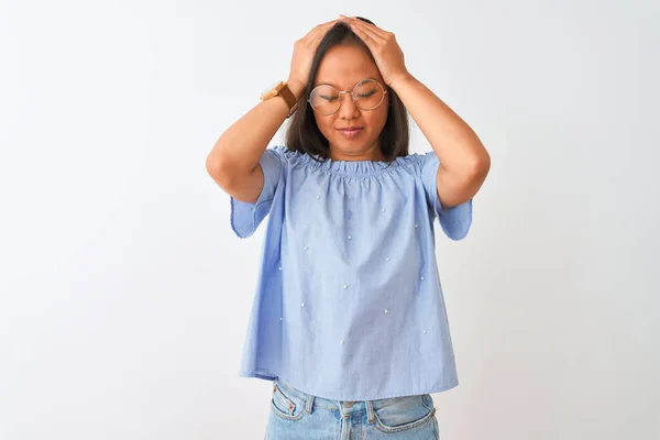 年轻的中国女人穿着蓝色的T恤 戴着眼镜 背负着孤立的白色背景 因疼痛和偏头痛而感到绝望和压力 手放在头上 — 图库照片