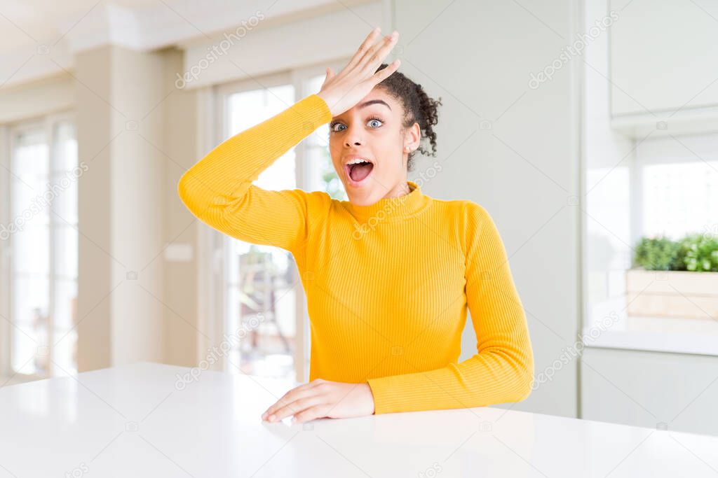 Beautiful african american woman with afro hair wearing a casual yellow sweater surprised with hand on head for mistake, remember error. Forgot, bad memory concept.
