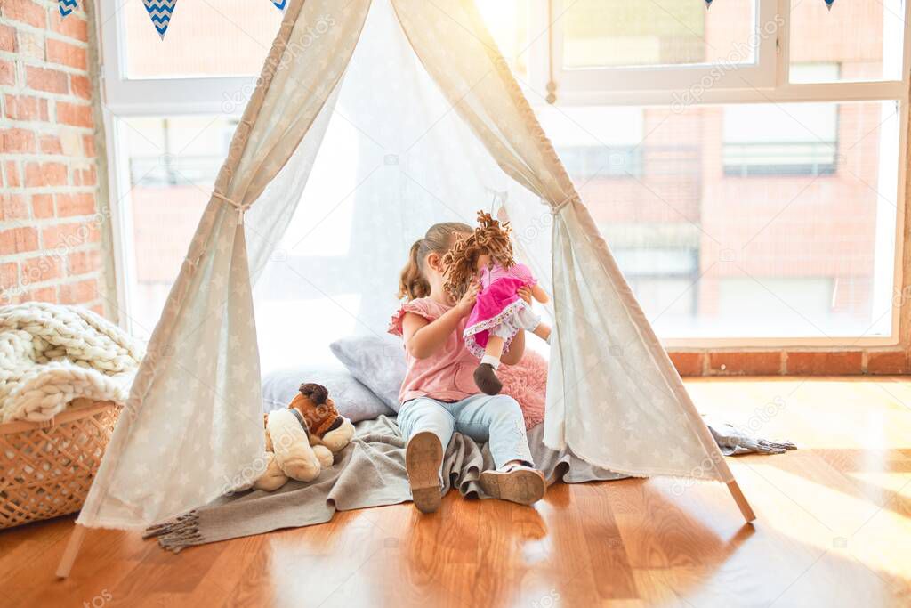 Beautiful blond toddler girl playing with dolls inside tipi at kindergarten