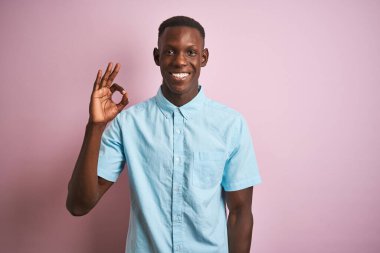 Mavi gömlekli Afro-Amerikan bir adam pembe arka planda dikiliyor ve el ve parmaklarıyla 
