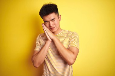 Asyalı genç bir Çinli tişört giyiyor. İzole edilmiş sarı arka planda duruyor. Uyuyor, yorgun uyuyor..