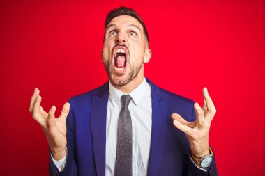 Genç ve yakışıklı iş adamı kırmızı arka planda çılgın ve kızgın bir şekilde bağırıyor ve agresif bir ifade ve kollarla bağırıyor. Hayal kırıklığı konsepti.
