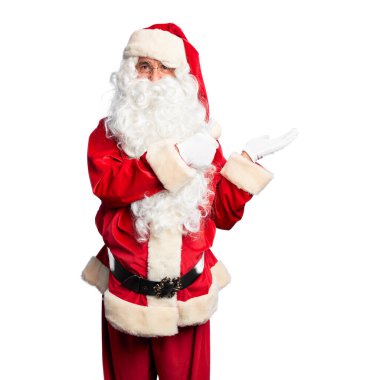 Orta yaşlı yakışıklı adam, Noel Baba kostümü ve sakal takıyor avuç içi gösteriyor ve baş parmaklarıyla hareket ediyor, mutlu ve neşeli gülümsüyor.