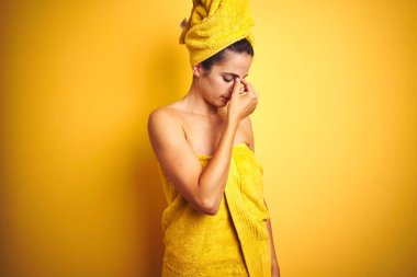 Vücuduna ve başına duş havlusu takan güzel bir kadın izole edilmiş sarı arka planda yorgun burnu ve gözleri ovuşturup yorgunluk ve baş ağrısı hissediyor. Stres ve hüsran kavramı.
