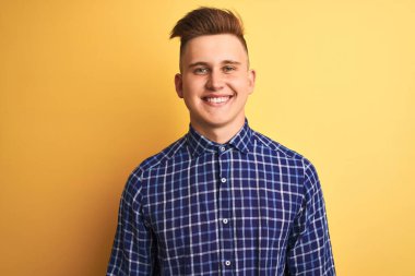 Yüzünde mutlu ve serin bir gülümsemeyle izole edilmiş sarı arka plan üzerinde duran sıradan tişört giyen genç yakışıklı bir adam. Şanslı kişi..