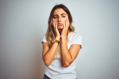 İzole edilmiş arka plan üzerinde günlük beyaz tişört giyen genç, güzel bir kadın. Yüzü, depresyonu ve üzüntüyü örten yorgun eller, sorun yüzünden üzgün ve sinirli.