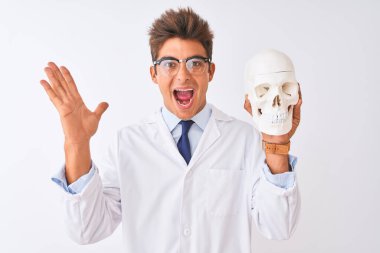 Gözlüklü yakışıklı doktor beyaz arka planda kafatasını tutuyor. Çok mutlu ve heyecanlı. Kazanan yüz ifadesi zaferi kutluyor.