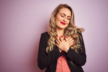 Güzel bir iş kadını pembe izole edilmiş arka planda duran zarif bir ceket giyiyor. Elleri göğsünde, gözleri kapalı ve yüzünde minnet dolu bir jest ile gülümsüyor. Sağlık kavramı.