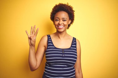 Beauitul Afrikalı Amerikan kadın izole sarı arka plan üzerine yaz t-shirt giyiyor ve parmak sayısı dört ile işaret kadar emin ve mutlu gülümseyen.