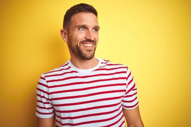 Sarı izole arka plan üzerine sıradan kırmızı çizgili tişört giyen yakışıklı bir adam yüzünde gülümseme, doğal bir ifade ile yan yana bakıyor. Kendinden emin gülen.
