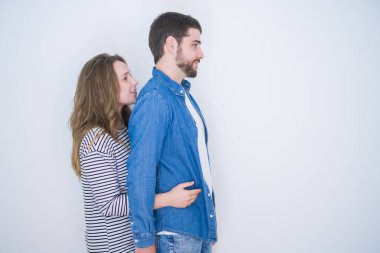 Genç ve güzel bir çift, beyaz izole edilmiş arka planda yan yana durur, rahat bir poz verir, kendine güvenen bir gülümsemeyle doğal bir poz verir..