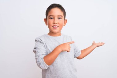 Gri günlük tişört giyen güzel bir çocuk izole edilmiş beyaz arka planda durup kameraya hayret ediyor ve gülümsüyor..