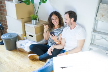 Orta yaşlı bir çift yeni bir eve taşınıyor. Akıllı telefon kullanıyor ve gülümseyen bir gülümsemeyle baş parmağıyla işaret ediyor.