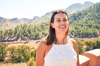Genç, güzel bir kadın dağ manzarasında yaz tatilinin tadını çıkarıyor, gezgin kız mutlu gülümsüyor.