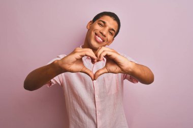 İzole edilmiş pembe arka plan üzerinde dikilmiş, elleri ile kalp sembolü şeklinde gülümseyen genç, yakışıklı Arap adam. Romantik konsept.