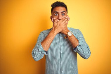 Yeşil çizgili tişört giyen genç Hintli adam izole edilmiş sarı arka planda dikiliyordu. Ağzını yanlışlıkla ellerle kapatıyordu. Gizli konsept.