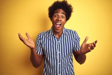 Afro saçlı, çizgili tişörtlü Amerikalı adam izole edilmiş sarı arka planda durmuş çılgın ve başarıyı kutlarken kolları havada ve gözleri açık heyecanlı bir şekilde haykırıyorlardı. Kazanan konsept