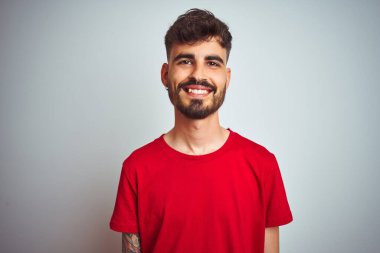 Yüzünde mutlu ve havalı bir gülümseme olan, izole edilmiş beyaz arka plan üzerinde duran kırmızı tişörtlü genç bir adam. Şanslı kişi..