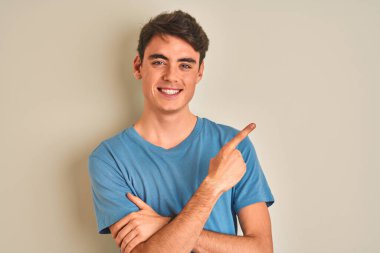 Sıradan tişörtler giyen genç bir çocuk izole edilmiş arka planda duruyor. Yüzünde kocaman bir gülümseme var. Elleri ve parmakları kameraya bakıyor..