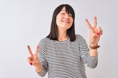 İzole edilmiş beyaz arka planda siyah çizgili tişört giyen güzel Çinli kadın kameraya bakıp zafer işareti yaparken gülümsüyor. İki numara..