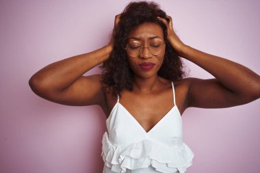 Young african american woman wearing glasses standing over isolated pink background suffering from headache desperate and stressed because pain and migraine. Hands on head.