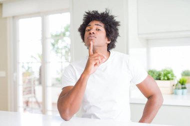 Genç Afro-Amerikalı bir adam, günlük beyaz tişörtler giyip evinde oturmuş, parmakları çenesinde şüpheye konsantre olmuş ve kafasını kaldırıp,