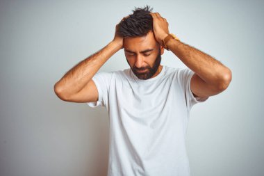 Genç Hint adam t-shirt ayakta baş ağrısı çaresiz ve vurguladı çünkü ağrı ve migren nedeniyle izole beyaz arka plan üzerinde duran giyiyor. Eller baş.