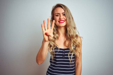 İzole edilmiş beyaz arka plan üzerinde duran çizgili tişört giyen genç ve güzel bir kadın kendini beğenmiş ve mutlu bir şekilde gülümserken dört numarayı işaret ediyor..