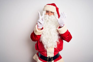 Noel Baba kostümü giymiş orta yaşlı yakışıklı adam izole edilmiş beyaz arka plan üzerinde duruyor ve yedinci parmaklarıyla işaret ederken kendinden emin ve mutlu bir şekilde gülümsüyor..