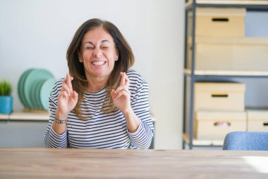 Orta yaş kıdemli kadın masada oturan evde işaret parmak umut ve gözler ile gülümseyen geçti kapalı. Şans ve batıl fikir.