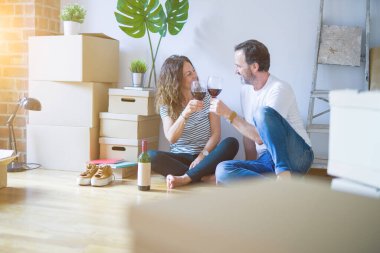 Orta yaş Senior romantik çift aşk yeni bir eve taşımak için mutlu gülümseyen bir bardak şarap içme kutluyor, etrafında kutuları ile daire katında oturan
