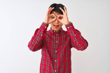 İzole edilmiş beyaz arka plan üzerinde duran sıradan kırmızı tişörtlü genç Çinli bir adam dürbün gibi dil çıkartıyor, gözler parmaklarından bakıyor. Çılgın ifade.