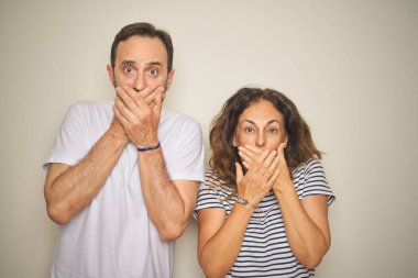 Güzel orta yaşlı çift, izole edilmiş beyaz arka planda dikiliyorlar. Ağızlarını yanlışlıkla elleriyle kapatıyorlar. Gizli konsept.