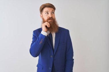 Genç kızıl saçlı İrlandalı işadamı, izole edilmiş beyaz arka planda dikilirken, elleri çenesinde soru sorarken, düşünceli bir ifade takınıyor. Düşünceli bir yüzle gülümsüyor. Şüphe kavramı.