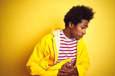 Afro saçlı Afro-Amerikalı bir adam, sarı arka planda duruyor, midesi bulanıyor, acı verici bir hastalığı var. Ache kavramı.
