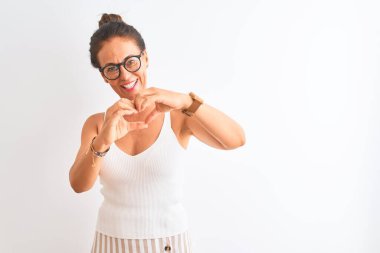 Sıradan tişörtler ve gözlük takan orta yaşlı bir kadın izole edilmiş beyaz arka planda duruyor. Aşkla gülümsüyor, elleriyle kalp sembolü yapıyor. Romantik konsept.