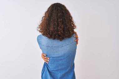 İzole edilmiş beyaz arka planda duran kot gömlekli genç Brezilyalı kadın kendine mutlu ve pozitif bir şekilde sarılıyor. Sevgi ve özgüven.