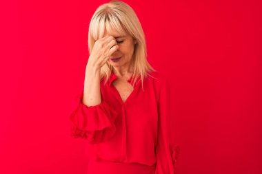Soyutlanmış kırmızı arka planda duran zarif gömlek giyen orta yaşlı kadın yorgun burnu ve gözlerini ovuşturup yorgunluk ve baş ağrısı hissediyor. Stres ve hüsran kavramı.