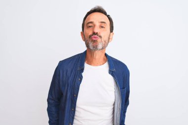 Mavi kot gömlek giyen orta yaşlı yakışıklı bir adam izole edilmiş beyaz arka planda dikilip kameraya bakarak havadan öpücük yolluyor ve çok seksi. Aşk ifadesi.