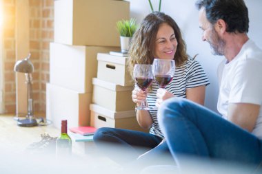 Orta yaş Senior romantik çift aşk yeni bir eve taşımak için mutlu gülümseyen bir bardak şarap içme kutluyor, etrafında kutuları ile daire katında oturan