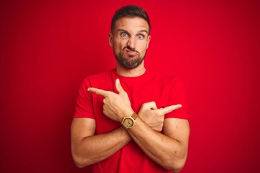Kırmızı izole edilmiş arka plan üzerine gündelik tişört giyen genç yakışıklı adam iki tarafı da parmaklarıyla işaret ediyor, farklı yönler farklı.